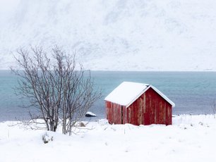 Kleines rotes Holzhaus in eingeschneiter Landschaft