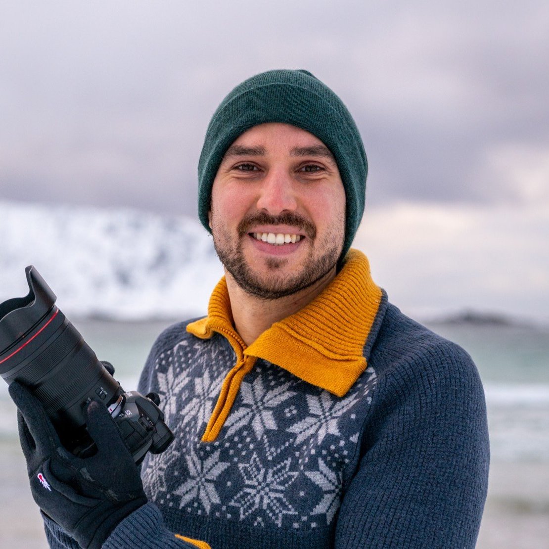 Fotograf Julien Pröpper mit Kamera in der Hand vor dem Meer
