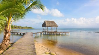 Ein Steg führt an einem Sandstrand ins Wasser zu einem Stelzenhaus