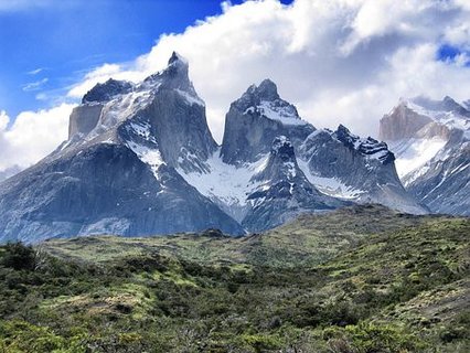 Patagonien Rundreise Selbstfahrer - Torres del Paine - Schroffe, schneebedeckte Berggipfel vor bewölktem Himmel und grün bewachsenem Hügel im Vordergrund