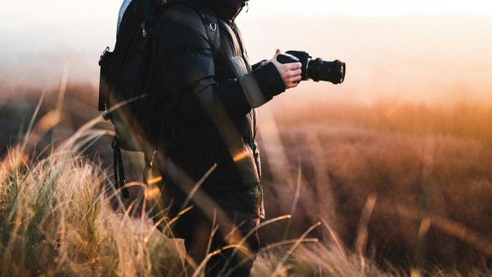 Mann hält Kamera in der Hand. Im Hintergrund ein schöner Sonnenuntergang