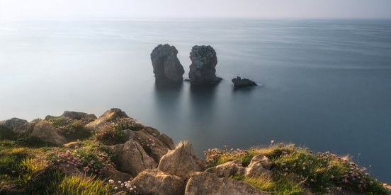 Aussicht von bewachsener Klippe auf Felsen die aus dem Meer ragen