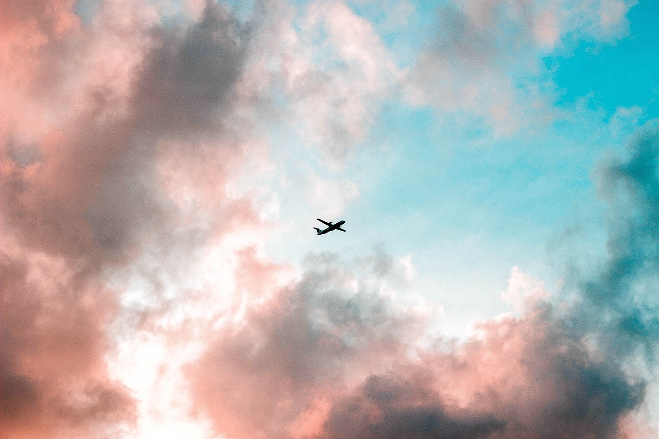 Flugzeug zwischen rosa Wolken und hellblauem Himmel