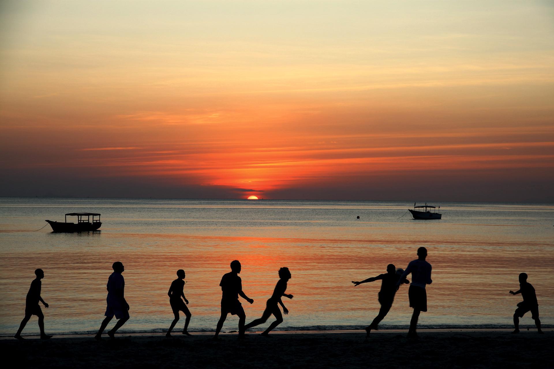 Fußballspielende Männer im Schatten der Abendsonne am Strand.