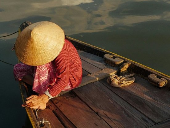 Frau kniet auf einem kleinen Holzboot im Licht der untergehenden Sonne