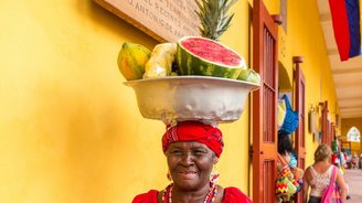 Einheimische Frau mit einer Schale voll Obst auf dem Kopf vor einer gelben Wand