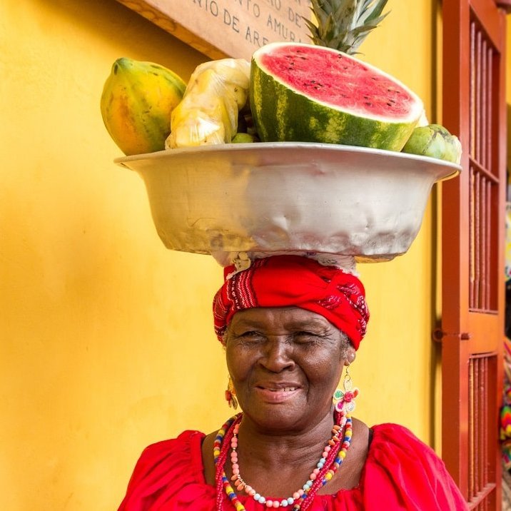 Einheimische Frau mit einer Schale voll Obst auf dem Kopf vor einer gelben Wand
