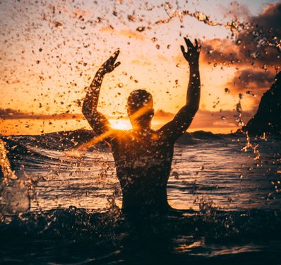 Mann im Meer spritzt mit Wasser bei Sonnenuntergang