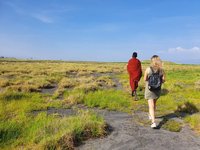 Eine Touristin folgt einem Massai durch die Savanne