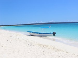 Boot liegt in weißem Sand bei türkisblauem Meer