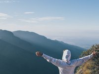 Mann mit Kapuzenpullover breitet seine Arme aus und schaut auf die Berge