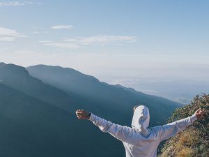 Mann mit Kapuzenpullover breitet seine Arme aus und schaut auf die Berge