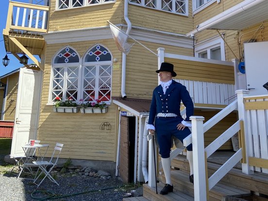 Traditionell gekleideter Finne vor einem gelben Haus