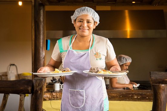 Köchin der La Tigra Rainforest Lodge mit zwei Tellern in der Hand lächelt
