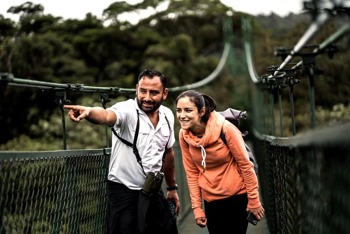 Reiseleiter Alvaro Jimenez zeigt einer Frau etwas während sie auf einer Hängebrücke stehen
