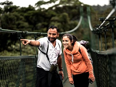 Reiseleiter Alvaro Jimenez zeigt einer Frau etwas während sie auf einer Hängebrücke stehen