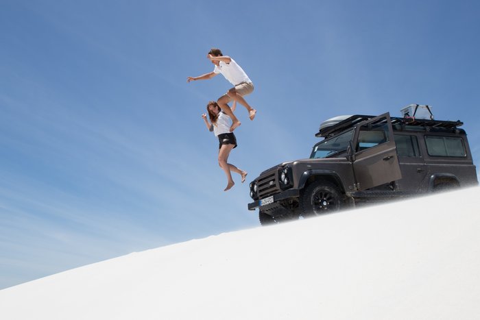 Menschen springen von einem Auto aus in den weißen Sand