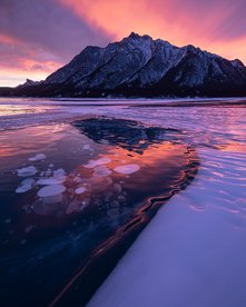 Pink.Lila Sonnenuntergang an einem zugefrorenen See mit Bergpanorama
