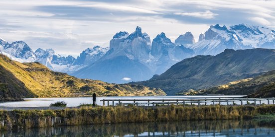 Person steht am Ufer einen Sees in dem sich die Berge im Hintergrund spiegeln bei Abendlicht