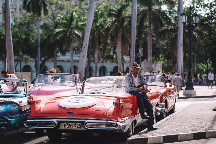 Mann mit Hut ist an Oldtimer gelehnt