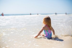 Mädchen im badeanzug sitzt am Strand und spielt in den Wellen