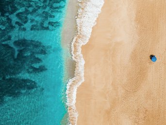 Mensch mit Sonnenschirm liegt am Strand