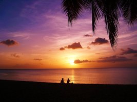 Zwei Menschen sitzen bei Sonnenuntergang am Strand und schauen aufs Meer