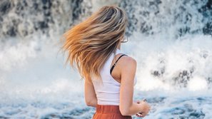Frau schwenkt ihre Haare vo einem Wasserfall