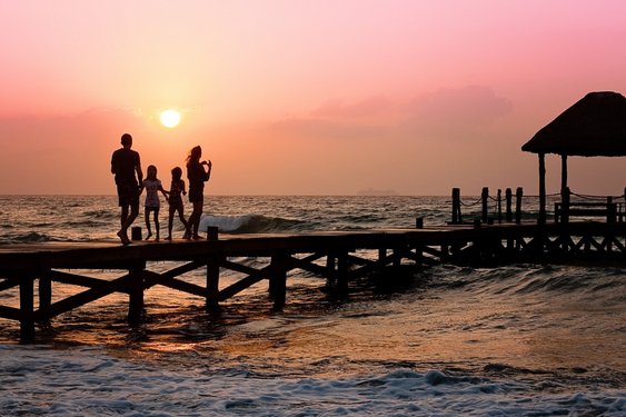 Familie auf einem Steg am Meer bei Sonnenuntergang