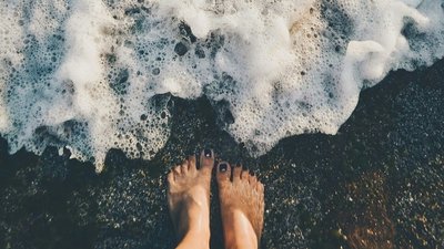 Füße im Sanstrand und Welle kommt