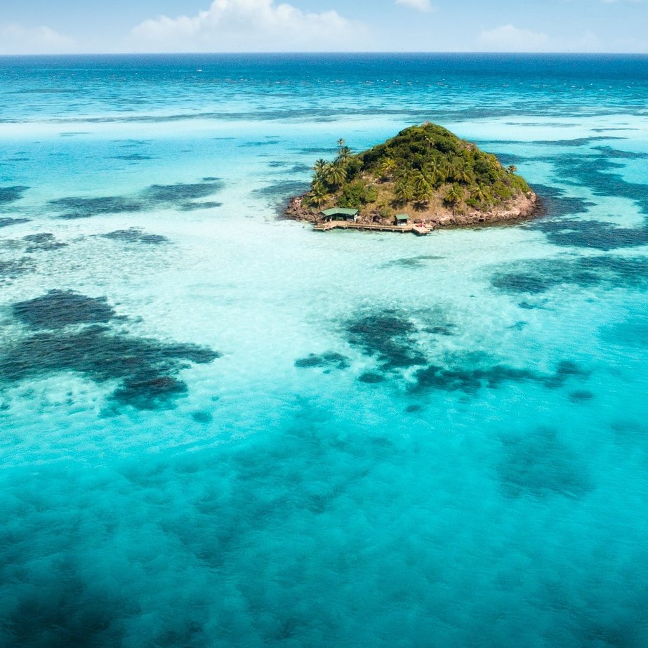 Eine kleine Insel in der Karibik umgeben von kristallklaren Wasser.
