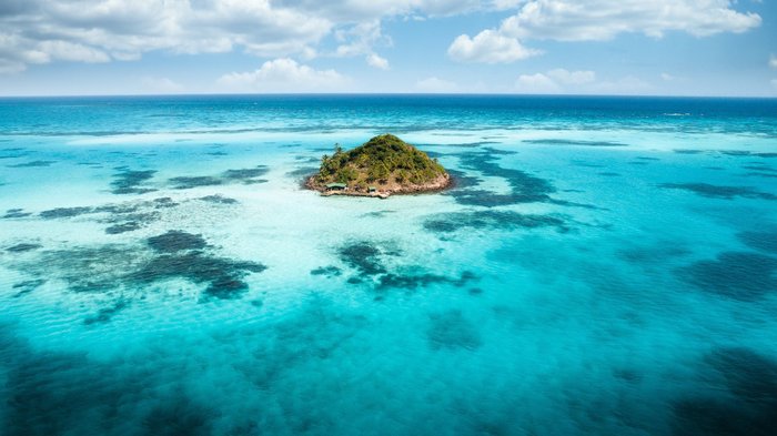 Eine kleine Insel in der Karibik umgeben von kristallklaren Wasser.