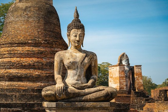 Sitzende Buddha Statue aus hellbraunem Stein vor Pagode