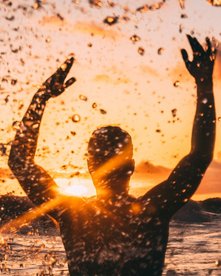 Mann im Meer spritzt mit Wasser bei Sonnenuntergang