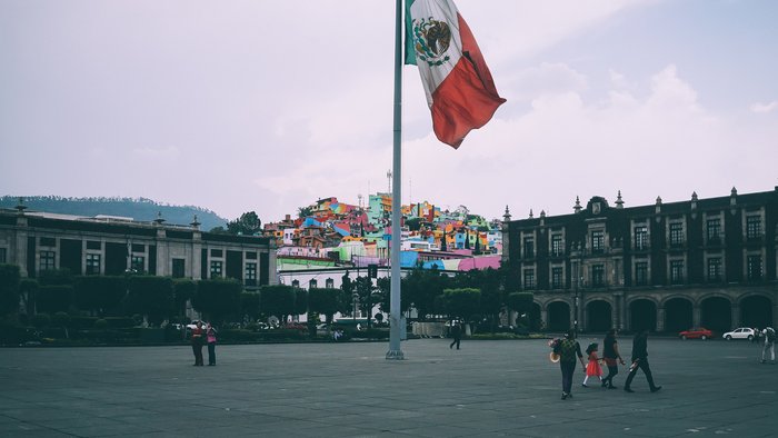 Bunt bemalte Häuser im Hintergrund und mexikanische Flagge im Vordergrund