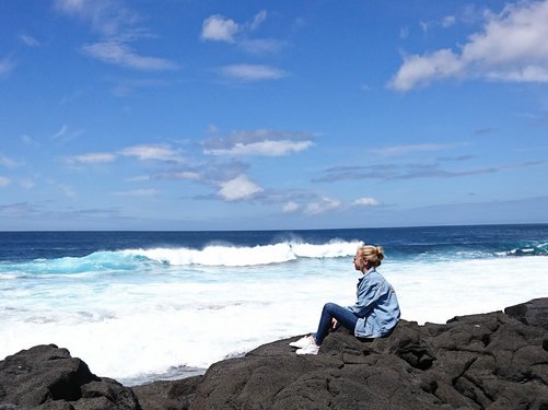 Frau mit Jeansjacke sitzt auf Felsen und schaut aufs Meer