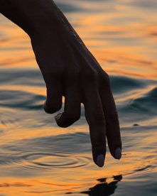 Hand nahe am Meerwasser bei Sonnenuntergang