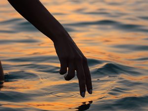Hand nahe am Meerwasser bei Sonnenuntergang