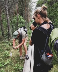 Eine Frau mit travel-to-nature Rucksack fotografiert eine Orchidee, die ihr der Guide zeigt