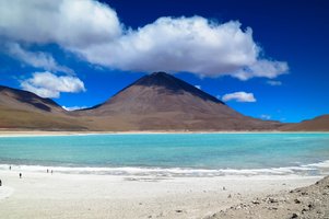Ein Berg hnter einem türkisblauen See in Bolivien mit einer weißen Schäfchenwolke