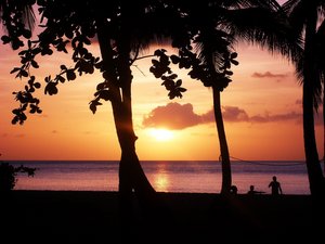 Strand bei Sonnenuntergang mit Palmen und Menschen