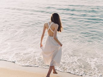 Frau in weißem Kleid läuft am Strand