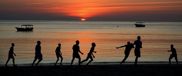 Fußballspielende Männer im Schatten des Sonnenuntergangs am Strand