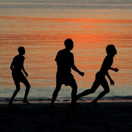 Fußballspielende Männer im Schatten der Abendsonne am Strand.
