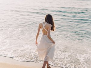 Frau in weißem Kleid läuft am Strand