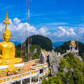 Goldene Buddha Statue auf Bergplateau vor blauem Himmel