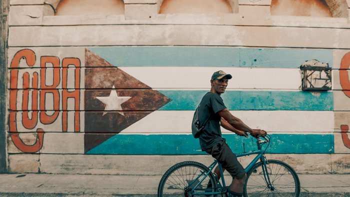 Mann mit Fahrrad posiert für Foto vor Kuba Flagge